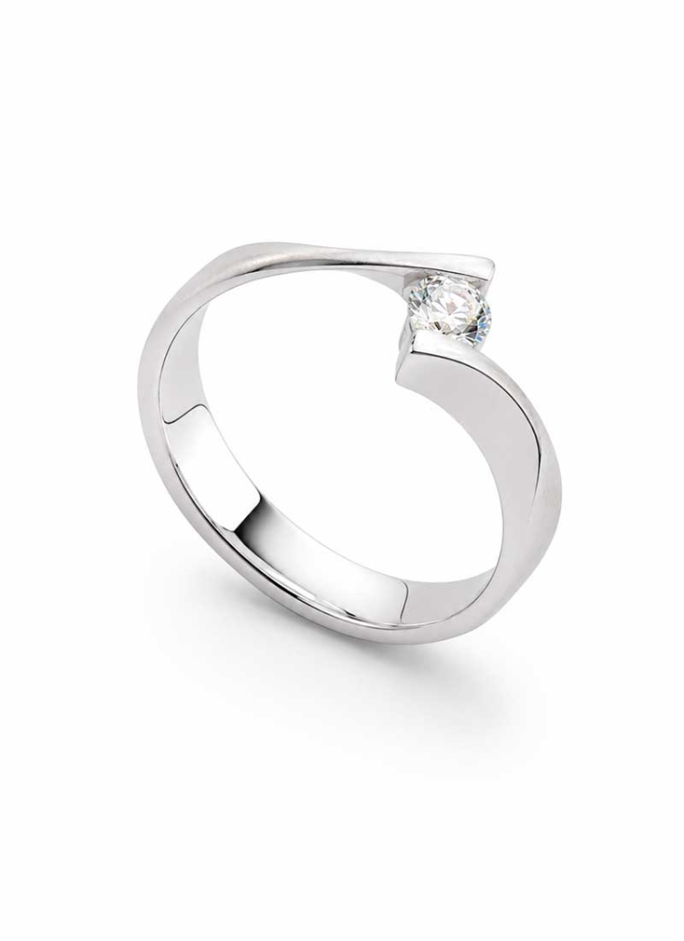 Original solitario cruzado con acabado mate en superficie central. Fabricado en oro blanco de 18Kt. Un diamante talla brillante 